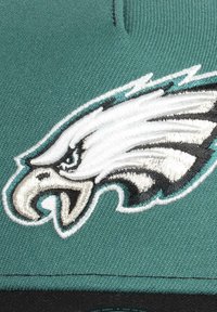 Eagles cap with a teal fabric, featuring an embroidered white and black eagle logo on the front. Smooth texture, structured design.