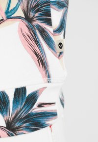 Sudadera con patrón floral que presenta grandes flores rosas y azules sobre un fondo blanco, con una pequeña etiqueta de marca en un lado.
