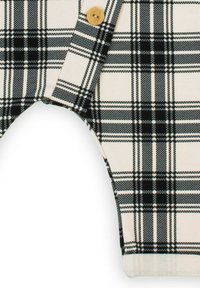 Tkanina w kratę czarno-białą na kremowym tle, z złotym guzikiem i zaokrąglonymi otworami na nogi. Widoczna jest fakturowana struktura tkaniny.