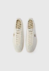 White leather sneakers with perforated details, lace-up design, and a gum sole. Gold logo accent visible on the outer side.