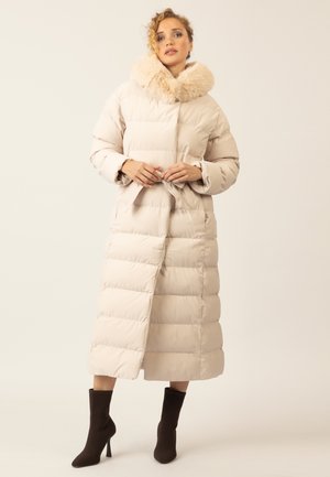 Beige Puffer-Jacke mit großem Kunstfellkragen, tailliertem Design und knielanger Länge. Verfügt über horizontale Steppabschnitte und lange Ärmel.