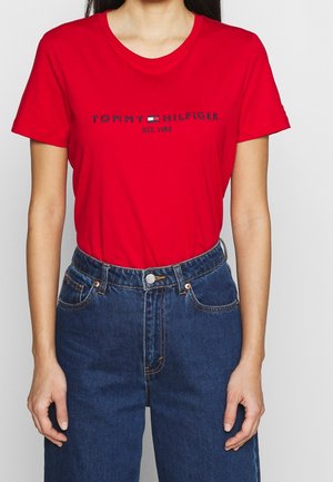 Czerwona bawełniana koszulka z okrągłym dekoltem, z logo "TOMMY HILFIGER" i rokiem założenia w ciemnym granacie. W połączeniu z wysokim stanem dżinsów.