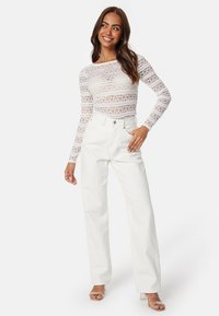 Top bianco in pizzo a maniche lunghe con pattern intricati e design aderente. Abbinato a jeans bianchi a vita alta, che sottolineano una vestibilità rilassata.