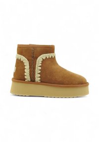 Stivale alla caviglia in suede marrone con punta arrotondata, cuciture decorative color crema e suola piatta beige. Presenta un accento intrecciato lungo il lato.