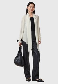 Ljuskrämfärgad cardigan med öppen front, texturerad stickning, kombinerad med svarta läderbyxor och en avslappnad svart handväska. Släta svarta platåskor.