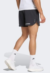 Men's black athletic shorts with reflective accents, lightweight fabric, side slits for mobility, paired with white socks and shoes.