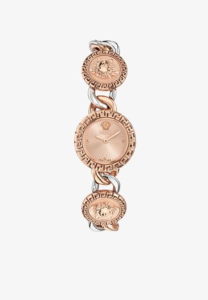 Reloj de metal dorado con esfera circular y patrones intrincados. Presenta eslabones con medallones florales y un logo central de Versace.