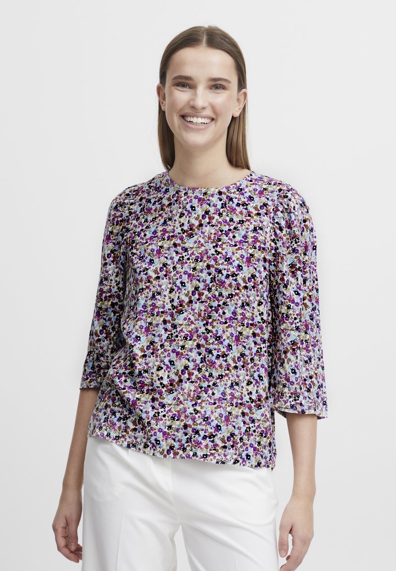 Floral blouse featuring a mix of purple, blue, and beige hues, bateau neckline, three-quarter sleeves, and a slightly loose fit.