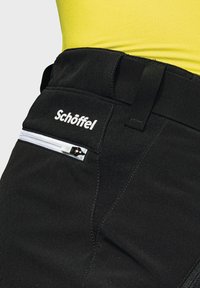 Schwarze Hosen mit glatter Textur, ausgestattet mit einer weißen Reißverschluss-Tasche und dem "Schöffel"-Logo am Bund. Einfaches Design, funktionale Details.