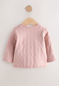 Pull bébé rose à manches longues avec un motif texturé ondulé, suspendu sur un cintre en bois sur un fond clair.