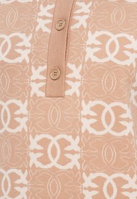 Top de malha com padrão bege, apresentando uma fileira de botões, com um design floral em creme mais claro, textura suave e trabalho de malha detalhado.