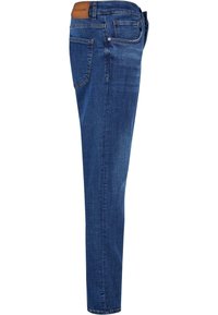 Jean en denim bleu vu de côté avec une poche arrière visible, une ceinture avec passants et un patch de marque en cuir.