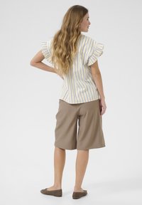 Top de rayas de manga corta en amarillo y azul con mangas con volantes, combinado con pantalones cortos marrones a la altura de la rodilla y calzado plano.