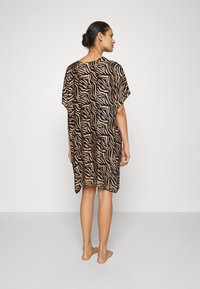 Kaftan con stampa animalier in beige e nero. Tessuto leggero, vestibilità ampia, maniche larghe e orlo al ginocchio. Presenta un design fluido.