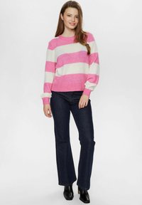 Rozā un baltu svītrains džemperis ar apaļu kakla izgriezumu un ribotām piedurknēm, apvienots ar tumši zilām plati izgrieztiem džinsiem un melniem potītiem zābakiem.