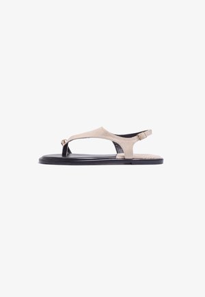 Sandale plate en daim beige avec semelle noire, bride entre les orteils et boucle ajustable à la cheville.