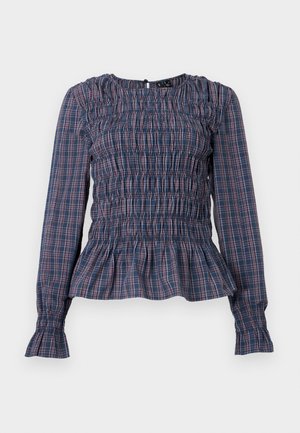 Blusa a maniche lunghe blu e rossa a quadri con corpino arricciato e orlo e polsini con volant, mostrata su uno sfondo bianco.