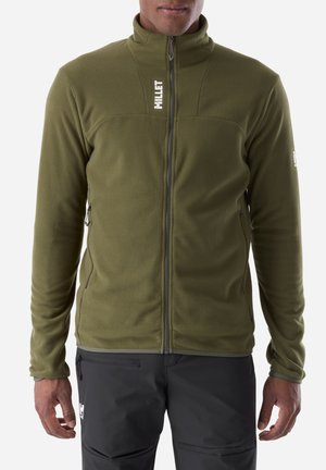 Mann trägt eine olivgrüne Fleecejacke mit Reißverschluss und weißem "MILLET" Logo auf der Brust sowie dunkelgraue Hose mit Reißverschlusstasche.