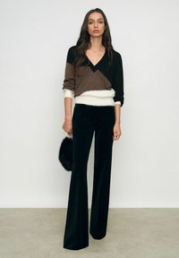 Pruun ja must värviline blokk-sviiter V-kaelusega, millele on paari pandud mustad flared-püksid. Modell hoiab ringikujulist musta, karvase tekstuuriga käekotti.