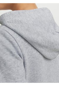 Gros plan d'une personne portant un sweat à capuche gris clair, montrant la capuche et la partie supérieure du dos avec une texture de tissu chiné doux.