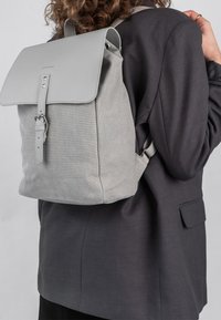 Šedý batoh s texturovaným tkaninovým tělem a hladkým koženým víkem. Obsahuje nastavitelné popruhy a kovovou sponu. Jednoduchý, moderní design.