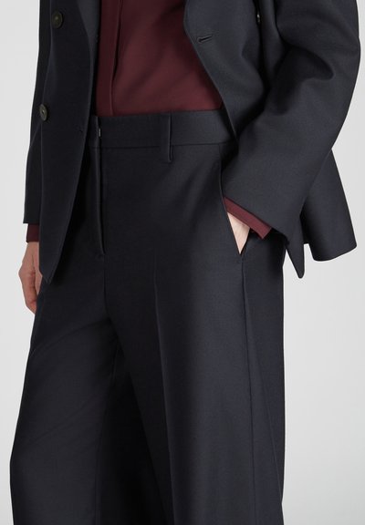 Pantalons de costume navy avec une texture lisse, jambe large, et une taille avec passants de ceinture, associés à un haut bordeaux avec un léger éclat.