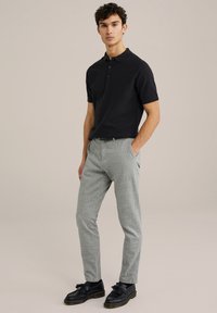 Tricou polo scurt negru, cu textură canelată, asortat cu pantaloni lungi tapered gri deschis și mocasini negri cu detalii din ciucuri.
