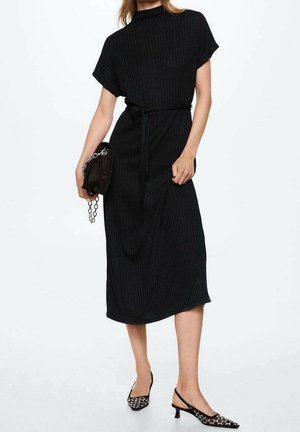 Černé žebrované midi šaty s vysokým límcem, krátkými rukávy a páskem v pase. Doplněné o černé sandály s páskem na patě se bílým vzorem.