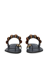 Sandalias planas negras con una distintiva correa curva adornada con acentos metálicos en bronce. Diseño abierto en los dedos con una estructura minimalista.