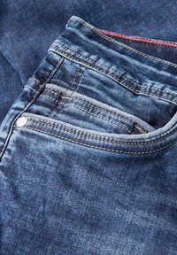 Jean en denim de couleur bleu délavé, doté de multiples poches, de coutures visibles et d'un petit détail de bouton argenté à l'avant.