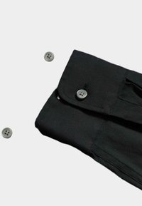 Colletto di camicia in tessuto nero con patta e dettagli di cucitura, caratterizzato da bottoni rotondi grigi sparsi.