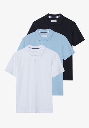 Trois polos en blanc, bleu clair et marine. Matière en coton, manches courtes, col avec patte de boutonnage à deux boutons et accents rayés sur le col.