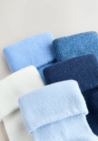 Cinco pares de calcetines de punto doblados en tonos de azul y blanco dispuestos de manera cercana y superpuesta sobre una superficie clara.