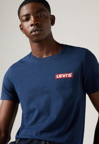 Tricou din bumbac de culoare bleu marin, cu un logo Levi's roșu dreptunghiular pe piept, mâneci scurte și un gât clasic rotund.