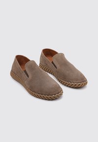 Zapatos de ante marrón tipo slip-on con diseño perforado, paneles laterales elásticos y costuras en contraste sobre una suela de goma texturizada.