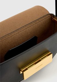Fekete bőrtáska barna velúr belsővel, arany színű kapoccsal és kontrasztos varrással, valamint vékony kártyazsebbel.