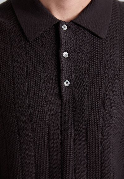 Zdravstvena slika temno pletenega polo majice s kragnico in tremi vidnimi svetlimi gumbi spredaj.