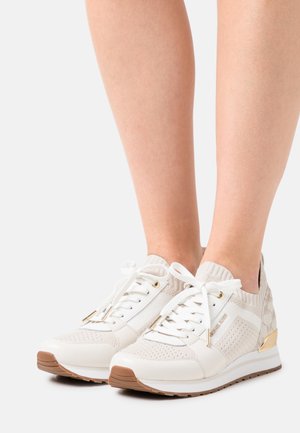 Sneakers bianchi con tomaia in maglia, design perforato e dettagli beige. Presentano chiusura con lacci e un sottile dettaglio metallizzato sul tallone.