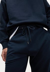 Navyblaues Sweatshirt mit Rundhalsausschnitt, kombiniert mit passenden Jogginghosen, die einen Kordelzugbund und dezente weiße Akzentuierungen an den Seiten aufweisen.
