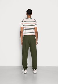 Gestreept t-shirt in wit, groen en roze; losse olijfgroene broek; gedragen met witte sneakers met zwarte en rode accenten.