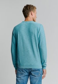 Turquoise gebreid sweater met een ronde hals, ribbelrand en textuurpatroon, gecombineerd met blauwe denim jeans. Zichtbare stiksels.