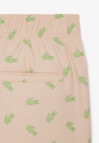 Beige Shorts mit elastischem Bund, grünen Krokodilmustern und einer einzelnen Gesäßtasche auf der rechten Seite.