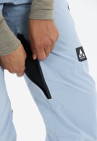 Ljusblå utomhusbyxor med zippered sidfickor, med meshfoder och en svart märkespatch, som visar upp en funktionell design.