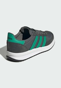 Baskets de sport grises avec trois bandes vertes, tige en suede et textile, semelle intermédiaire blanche et semelle extérieure en caoutchouc noir. Logo sur le talon.