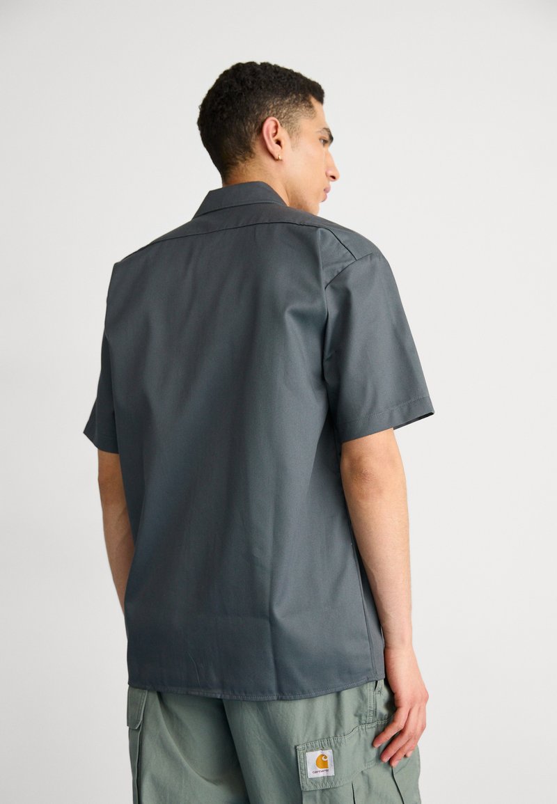 Camicia a maniche corte con colletto in grigio scuro, realizzata in tessuto liscio, vista da dietro. Presenta un taglio pulito e dettagli minimi.