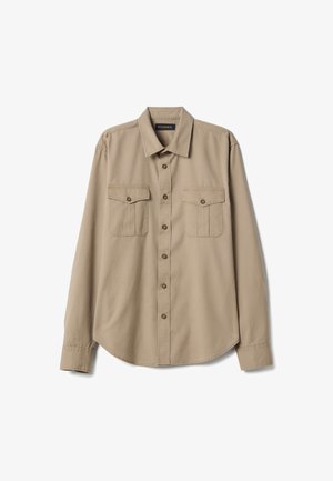 Camisa beige de manga larga con botones, cuello puntiagudo y dos bolsillos en el pecho con botones, extendida sobre un fondo blanco.