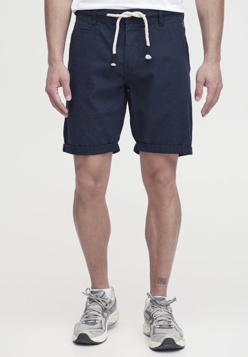 Pantalones cortos de algodón azul marino con dobladillos enrollados, con un cordón de ajuste blanco y bolsillos laterales. La textura es suave y ligera.