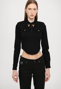 Black cropped denim jacket with long sleeves, gold triangular accents on collar, button closure, and two front pockets.