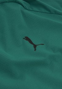 Tessuto verde con un motivo a rilievo, con una silhouette del logo Puma nera sulla superficie. Materiale morbido e leggero.