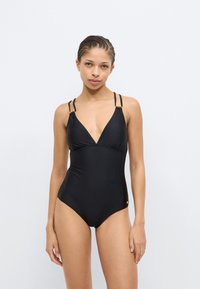 Juodas vientisas maudymosi kostiumėlis su gilia V formos iškirpte, plonomis dvigubomis petnešėlėmis ir auksiniais akcentais. Lygus, tamprus audinys su prigludusia silueto linija.